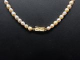 a white pearl necklace with a gold clasp on a mannequin