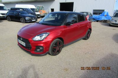 La petite voiture rouge est garée sur un parking avec d'autres voitures.