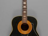 an old black acoustic guitar sitting on top of a gray surface