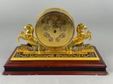 a gold clock on a wooden base with two horses on it