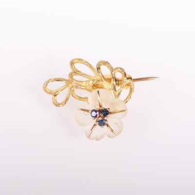 un gros plan d'une broche en forme de fleur en or sertie de pierres bleues