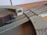 un train miniature sur les rails, avec un petit bâtiment en arrière-plan