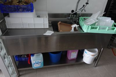 un évier en inox dans une cuisine où l'on trouve beaucoup de produits d'entretien