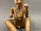wooden statue of a man sitting on the ground with his hands in the air