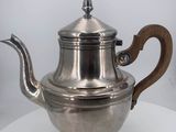 an antique silver tea pot with a wooden handle on a table