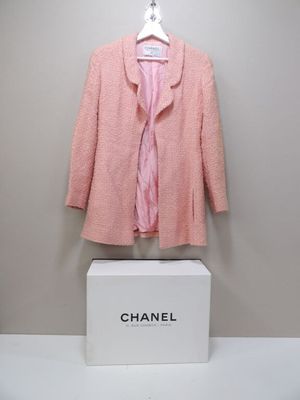 Une veste en tweed rose Chanel et une chemise rose exposées dans une boîte blanche