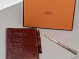 un portefeuille en cuir marron et un stylo posés sur une table, à côté d'une boîte