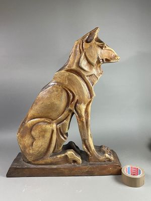 une statue représentant un chien assis sur un socle, à côté d'un ruban