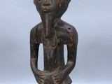 une vieille statue en bois représentant une femme, les mains dans les poches