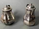 two silver teapots sitting on a gray surface