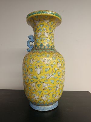 a yellow vase sitting on a table with a blue bird on it
