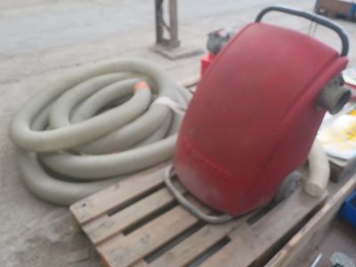un réservoir rouge posé sur une palette, à côté d'un tuyau