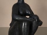 statue d'une femme assise sur une table en verre, les mains posées sur les genoux