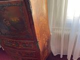 a wooden cabinet with a painting on it next to a window