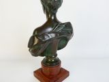 buste en bronze représentant une femme, posé sur un socle en bois, avec un fond blanc