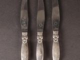 three silverplated knives and a knife holder on a black surface