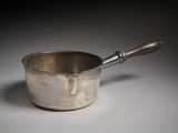 une casserole en argent avec un manche en bois posée sur une table