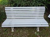 a white bench sitting in the grass next to a bush