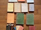 Plusieurs livres sont disposés sur un plancher en bois, à côté d'une pile de papiers