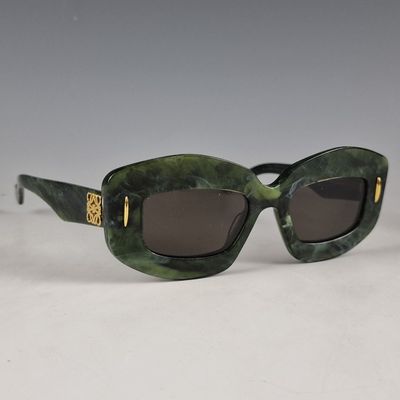 des lunettes de soleil vertes aux verres marron posées sur une surface blanche