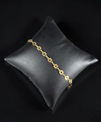 un bracelet en chaîne d'or posé sur un coussin, sur fond noir