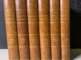 six livres anciens reliés en cuir, alignés sur une table blanche