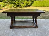 une table en bois sur une terrasse en pierre, avec un buisson en arrière-plan