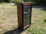 une vieille armoire en bois avec une porte vitrée, posée dans l'herbe