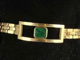 a close up of a gold bracelet with a green stone on it