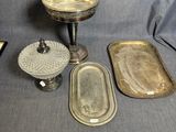 trois plateaux en argent et une assiette en argent posés sur une nappe grise