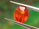 un gros plan sur un diamant orange tenu par une paire de pinces