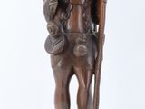 an old wooden statue of a man holding a stick and a bag