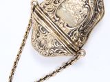 un vieux porte-monnaie en argent, entouré d'une chaîne, posé sur une surface blanche