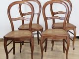 four wooden chairs with wicker seats in a row against a white wall