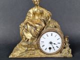 une statue représentant une femme assise sur un rocher, avec une horloge devant elle
