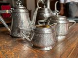 four silver teapots on a wooden table with a man in the background