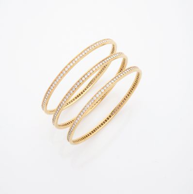 une pile de trois bracelets rigides en or et diamants sur fond blanc