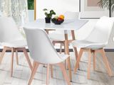 une table blanche avec quatre chaises et un bol de fruits posé dessus