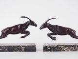 deux statues de béliers en train de courir, posées sur des socles en marbre, sur fond blanc