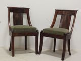 Deux chaises en bois, dotées de coussins rembourrés verts, sont adossées à un mur blanc.