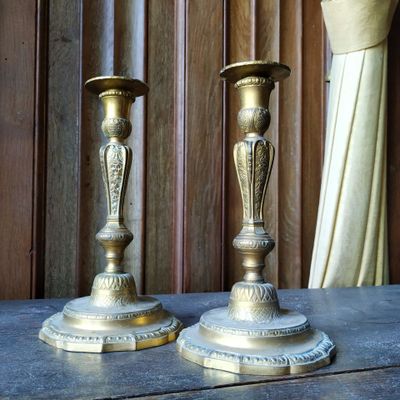 une paire de bougeoirs anciens en laiton posés sur une table devant un rideau