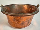 une grande casserole en cuivre avec des poignées, posée sur une surface blanche