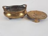 deux petits pots en laiton avec leurs couvercles, posés sur une surface blanche