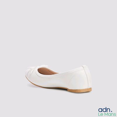 La femme porte des chaussures blanches ornées d'un nœud sur le côté.