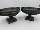 une paire d'urnes anciennes en fonte posées sur des socles, sur fond blanc