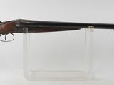 un fusil posé sur un socle transparent, devant un fond blanc