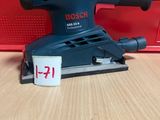 un gros plan d'une ponceuse posée sur une table, avec une boîte rouge en arrière-plan