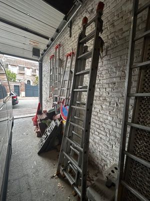 plusieurs échelles appuyées contre un mur de briques, à côté d'une camionnette