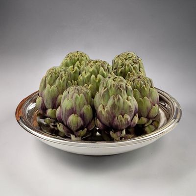 four artichokes in a silver bowl on a table