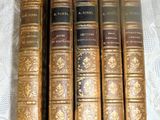 six old books are lined up on a white table cloth